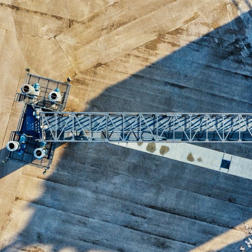Drone capture of an industrial crane casting shadows on a construction site in bright sunlight.